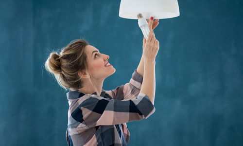 Woman changing a light bulb removing a compact fluorescent energy saving bulb against a blue background