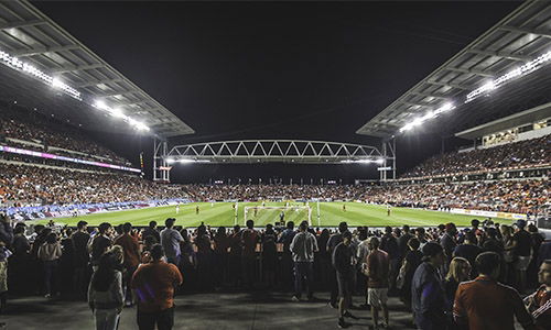 Football stadium filled with fans at night with bright lights illuminating the pitch