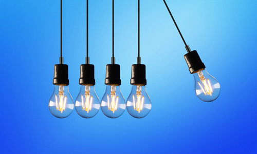 Light bulbs in a socket infront of a blue background with black pendants and swinging like newtons cradle